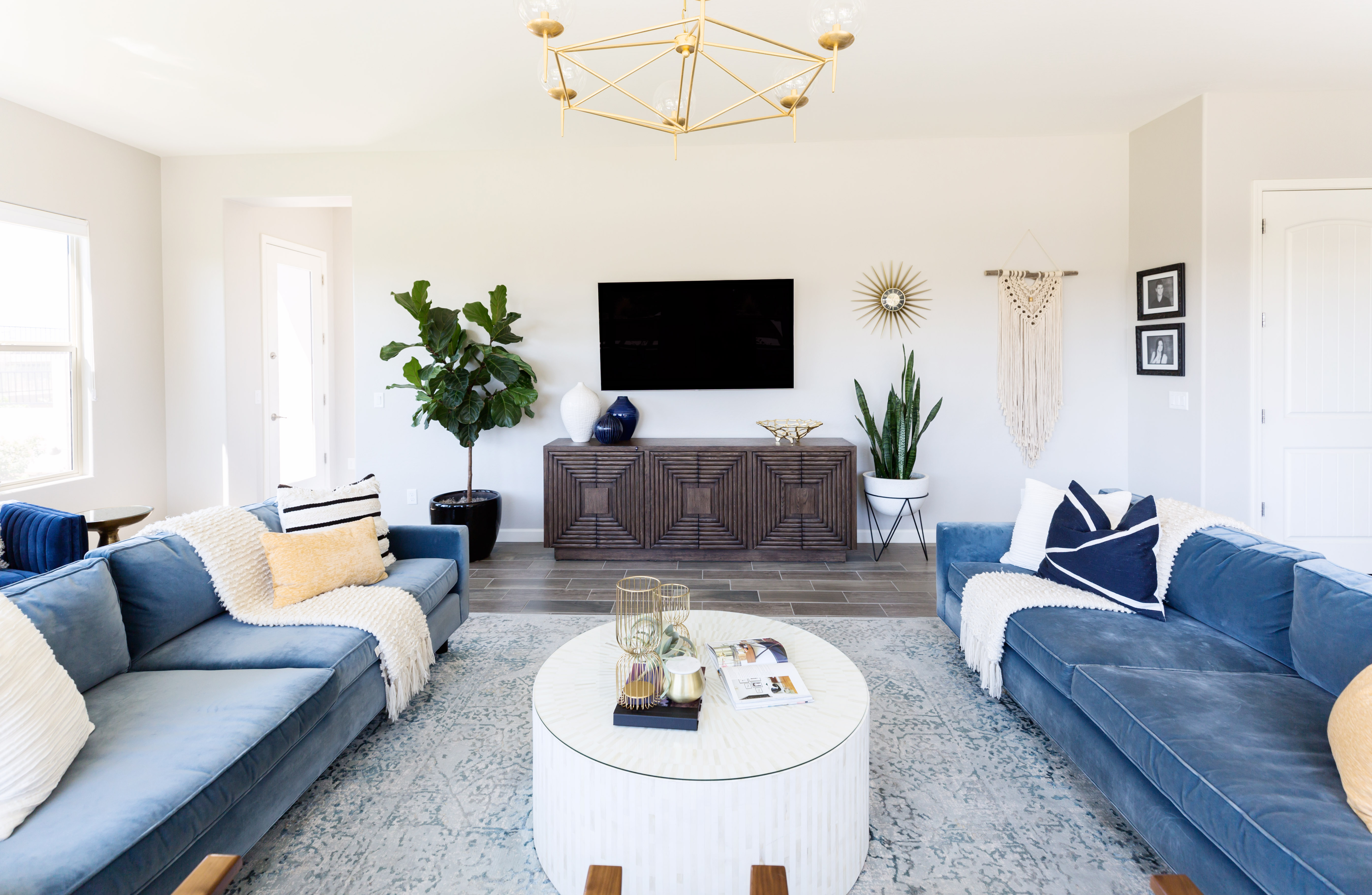 A living room with a TV on a white wall, facing the seating f two blue sofas