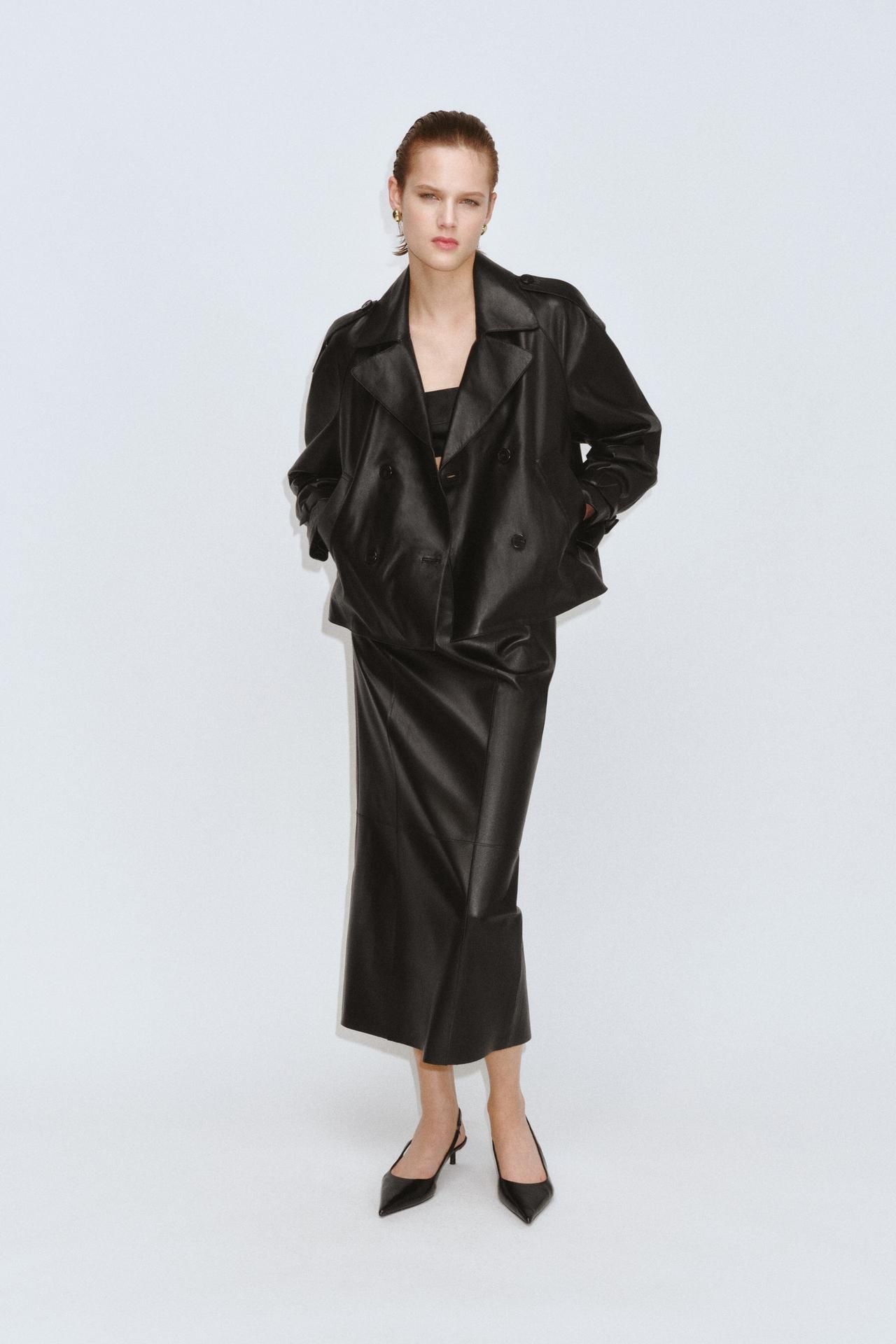 Model wears leather midi skirt and cropped trench set with sling backs.