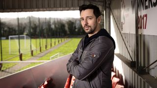 Ralf Little in Who Do You Think You Are on the stands at Chirk FC football ground in Wales, wearing a black coat