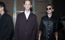 Male models in dark clothing prepare for fashion show