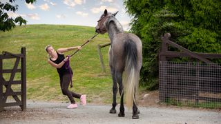 Lady trying to pull horse through a gate