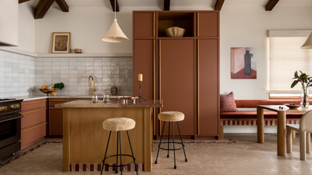 A warm muted terracotta kitchen in a modern traditional style with high ceilings and exposed beams, built in banquette seating and a striped accent for areas like the plinth.