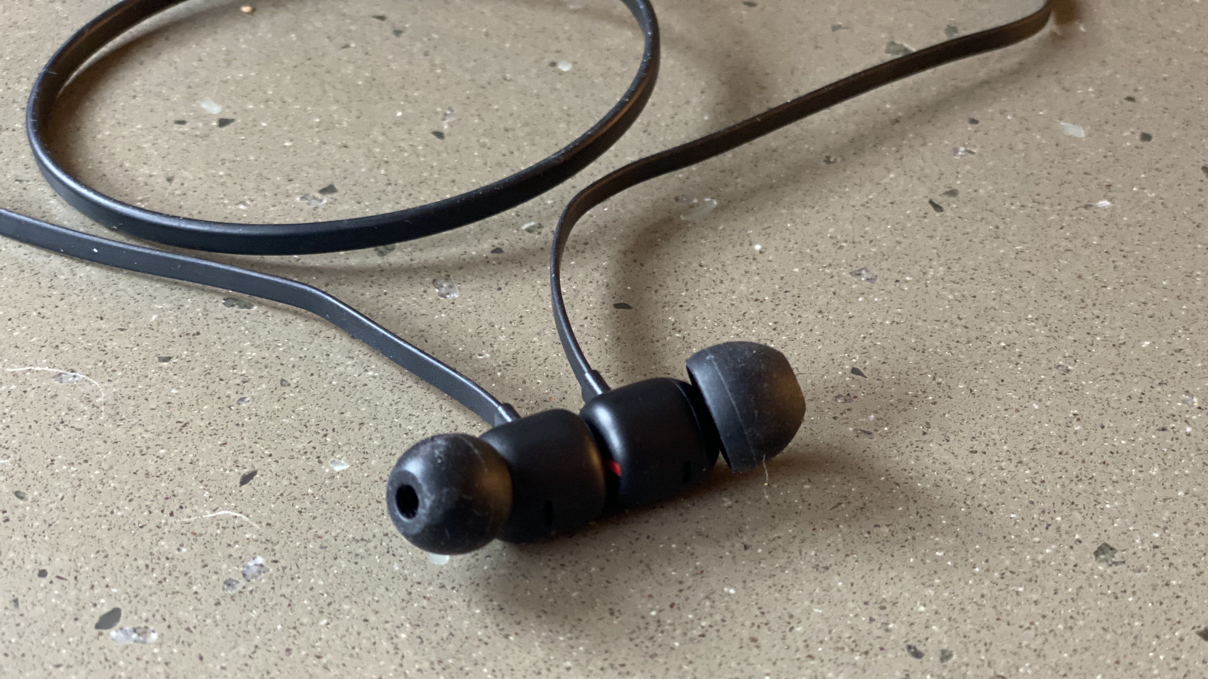 Tampilan dekat earbud earphone nirkabel Beats Flex berwarna hitam di atas permukaan marmer