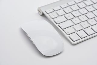 A white Apple Magic Mouse next to a white and gray Apple Magic Keyboard, both on a white surface
