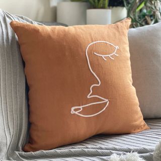 Fall throw pillow with embroidered face on on cream sofa 