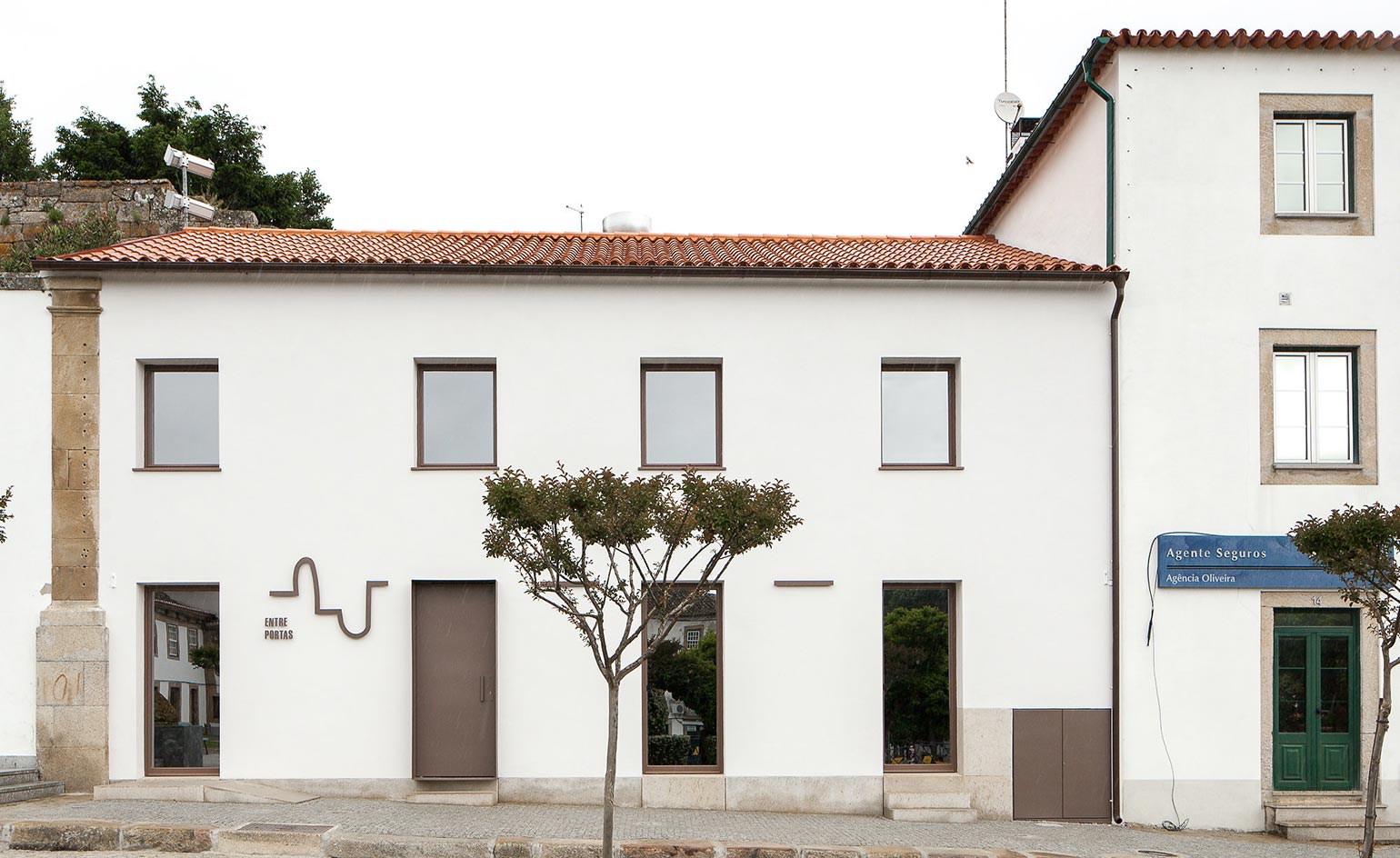 Exterior view of the Entre Portas restaurant. White, two-floor building, with brown doors and window panes. A tree is next to the sidewalk.