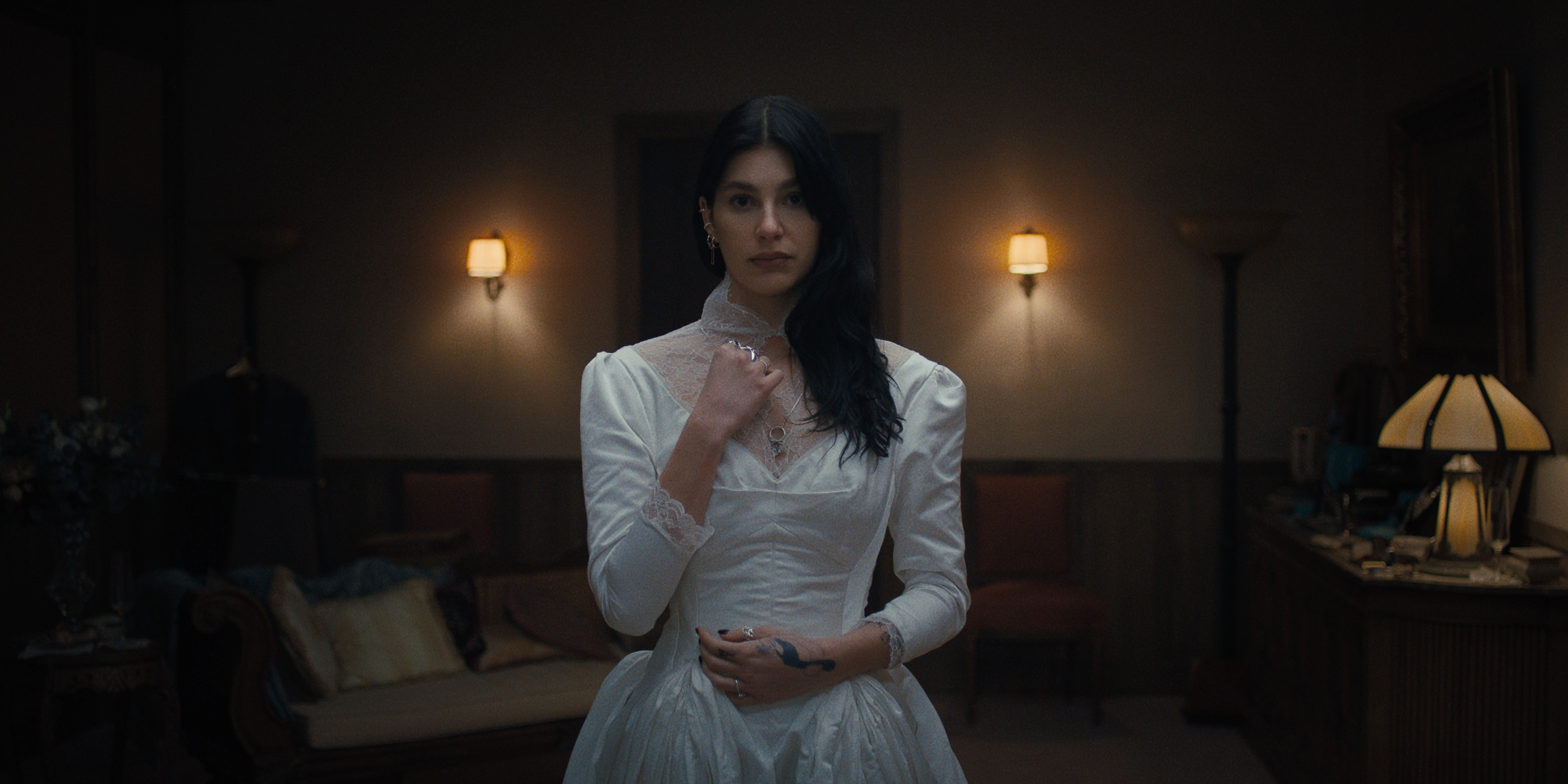 Camila Morrone as Rachel Harkin in episode 102 of Something Very Bad Is Going To Happen trying on an old looking wedding gown in a dark room