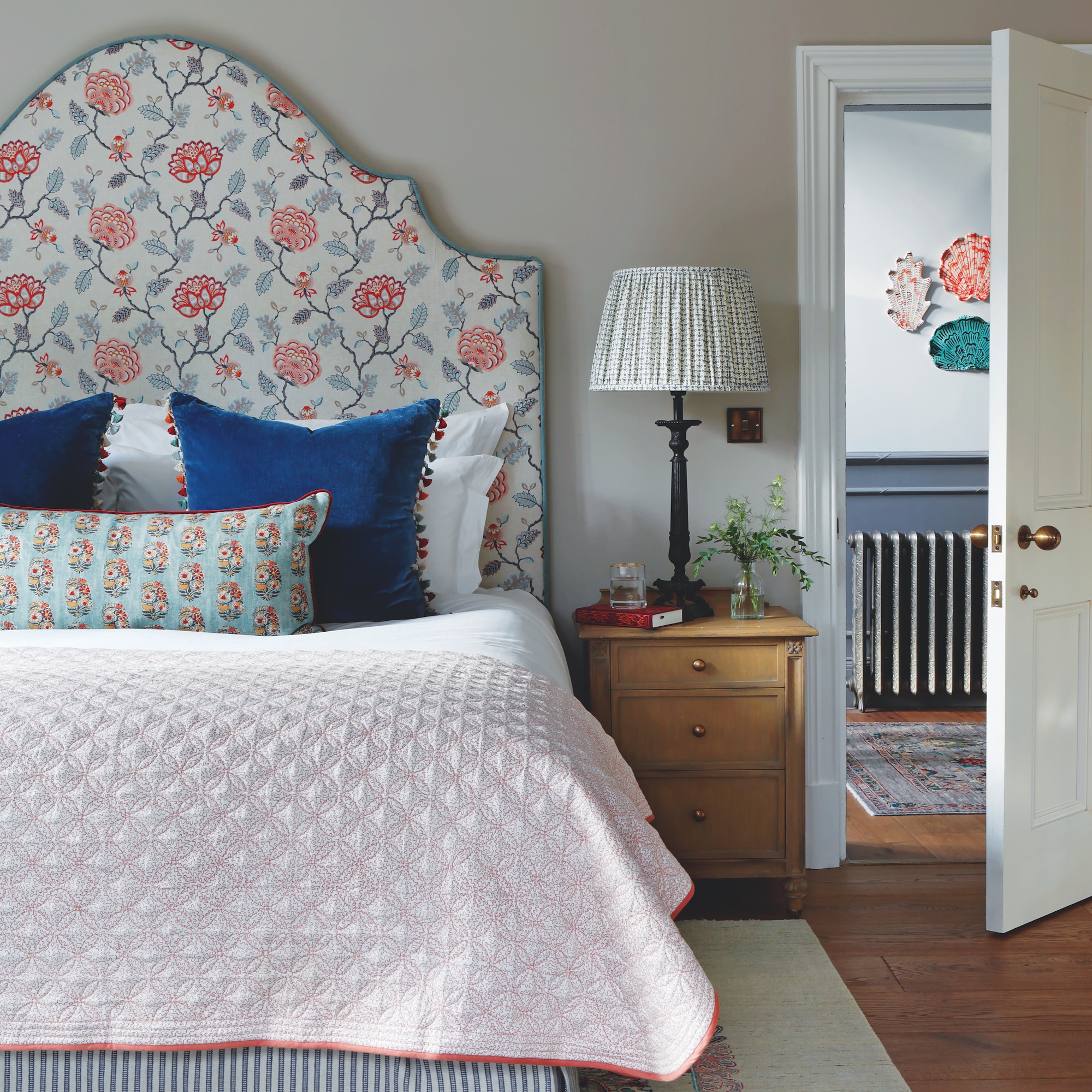 bedroom with large shaped headboard covered in floral fabric, with wooden bedside drawers and lamp