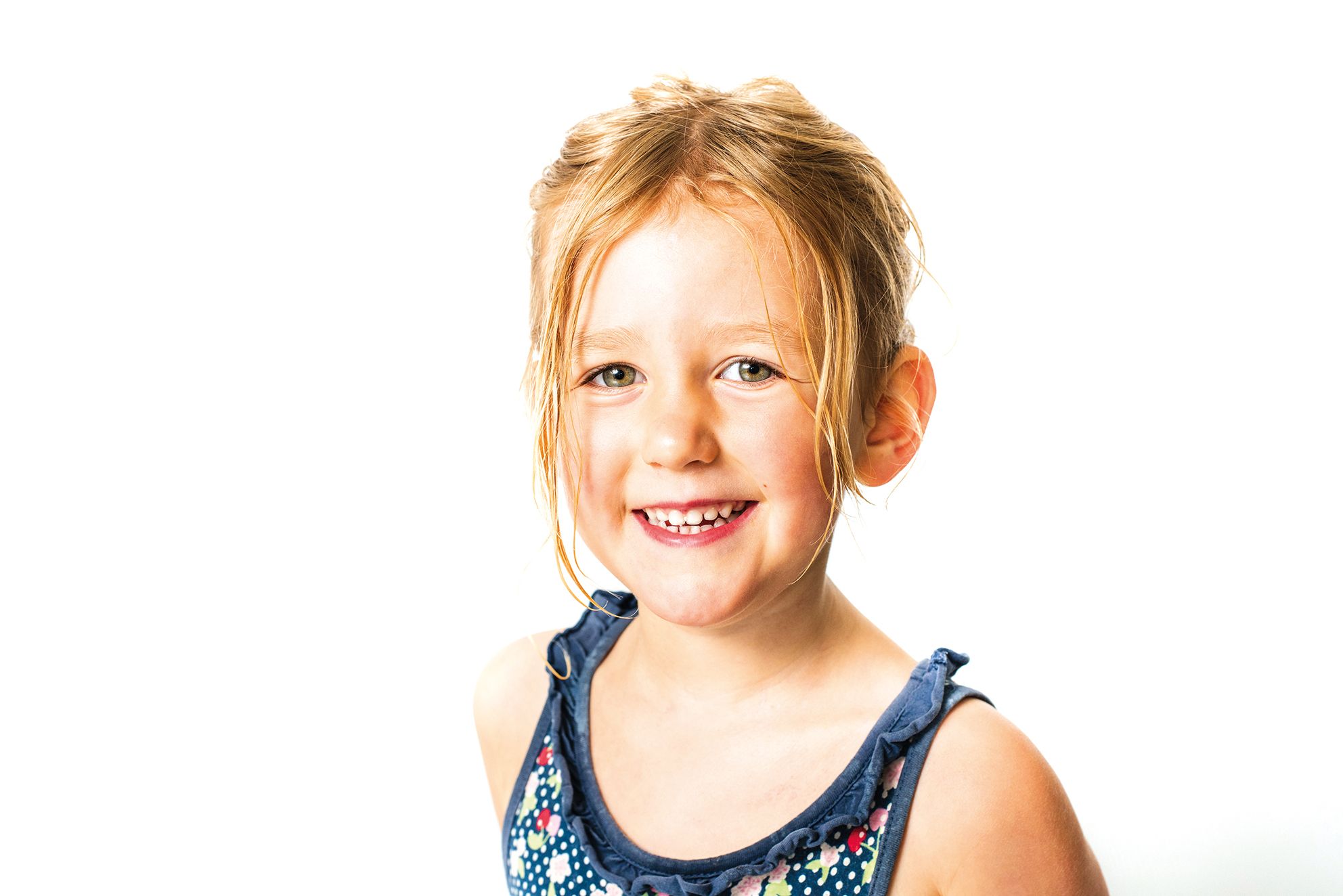 A child with blonde hair, dressed in a navy top with colorful patterns, poses against a bright white background