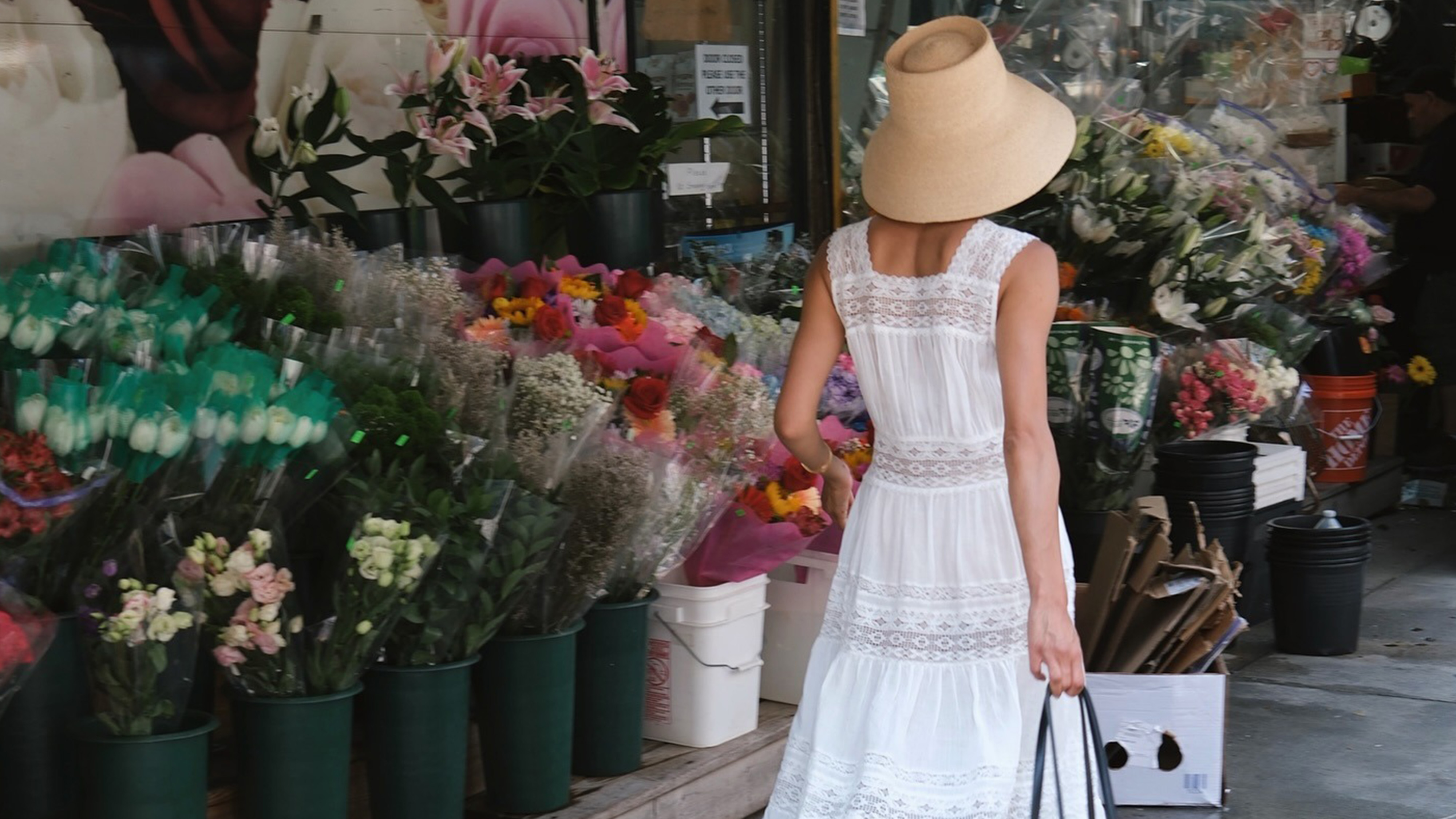 Shay wears a straw hat and white lace-trim maxi dress.
