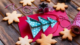 Folded christmas tree in blue and white spotted paper set on a red card surrounded with snowflake-shaped biscuits