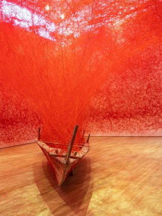 A wooden boat covered in red string which extends to the walls and ceiling