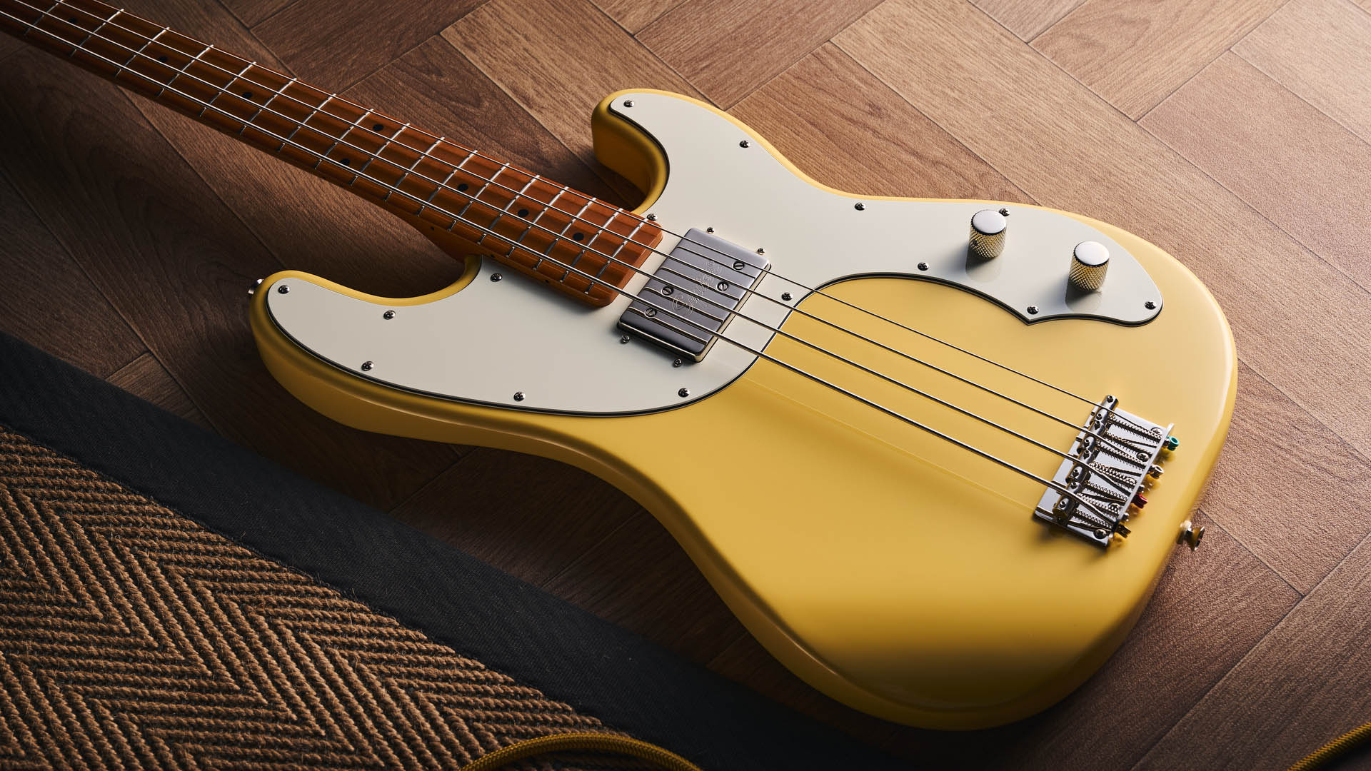 The Squier Classic Vibe Telecaster Bass is a fine-looking four-string in a custard-colored Vintage White, and is here photographed in close-up, against a plain wooden background. It has a single Wide Range humbucker.