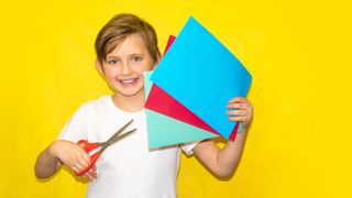 Young boy holding a fan display of coloured paper and a pair of scissors
