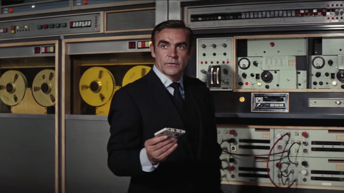 Sean Connery holding a cassette tape in front of an old school computer in Diamonds Are Forever.