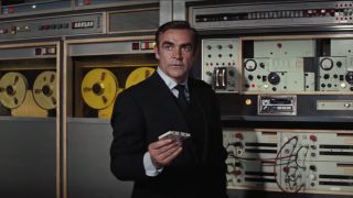 Sean Connery holding a cassette tape in front of an old school computer in Diamonds Are Forever.