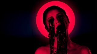 A woman bathed i nred light with VHS reel coming out of her eyes and mouth