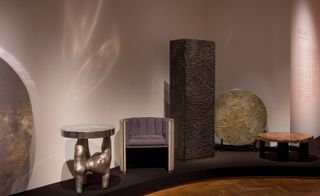 The eclectic display of works demonstrate Chale’s penchant for abstract decoration. A silver round coffee table, a round chair, a cupboard with a rough surface, a round gold decoration and round brown marble coffee table on a raised platform.