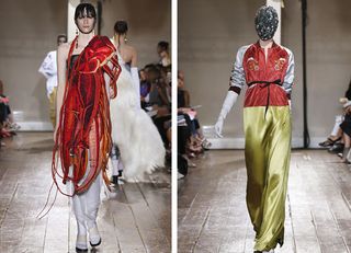 Two female catwalk models wearing red, grey and gold theme designer outfits, wooden floor, neytral wall background, audience sat in chairs either side of the catwalk watching the models