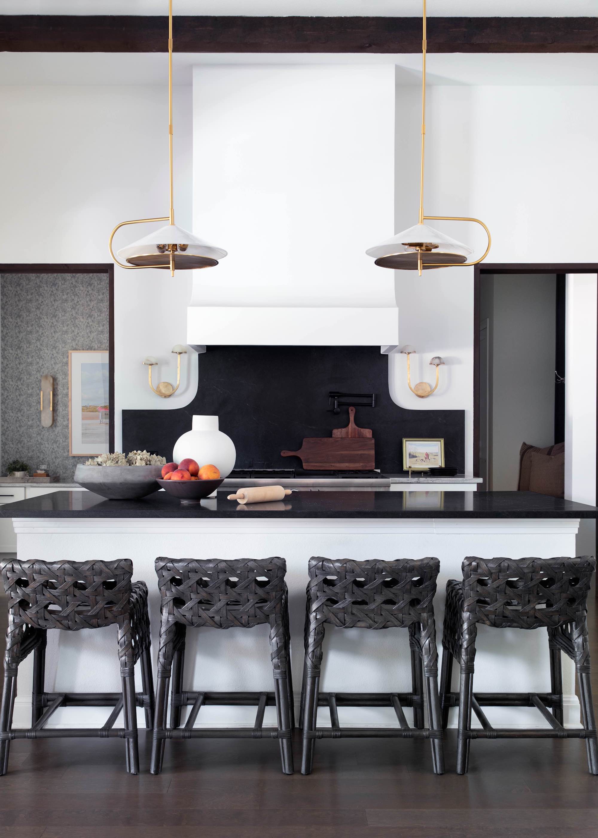 white and black kitchen with brass light fittings above a large kitchen island and next to the island are four bar stools