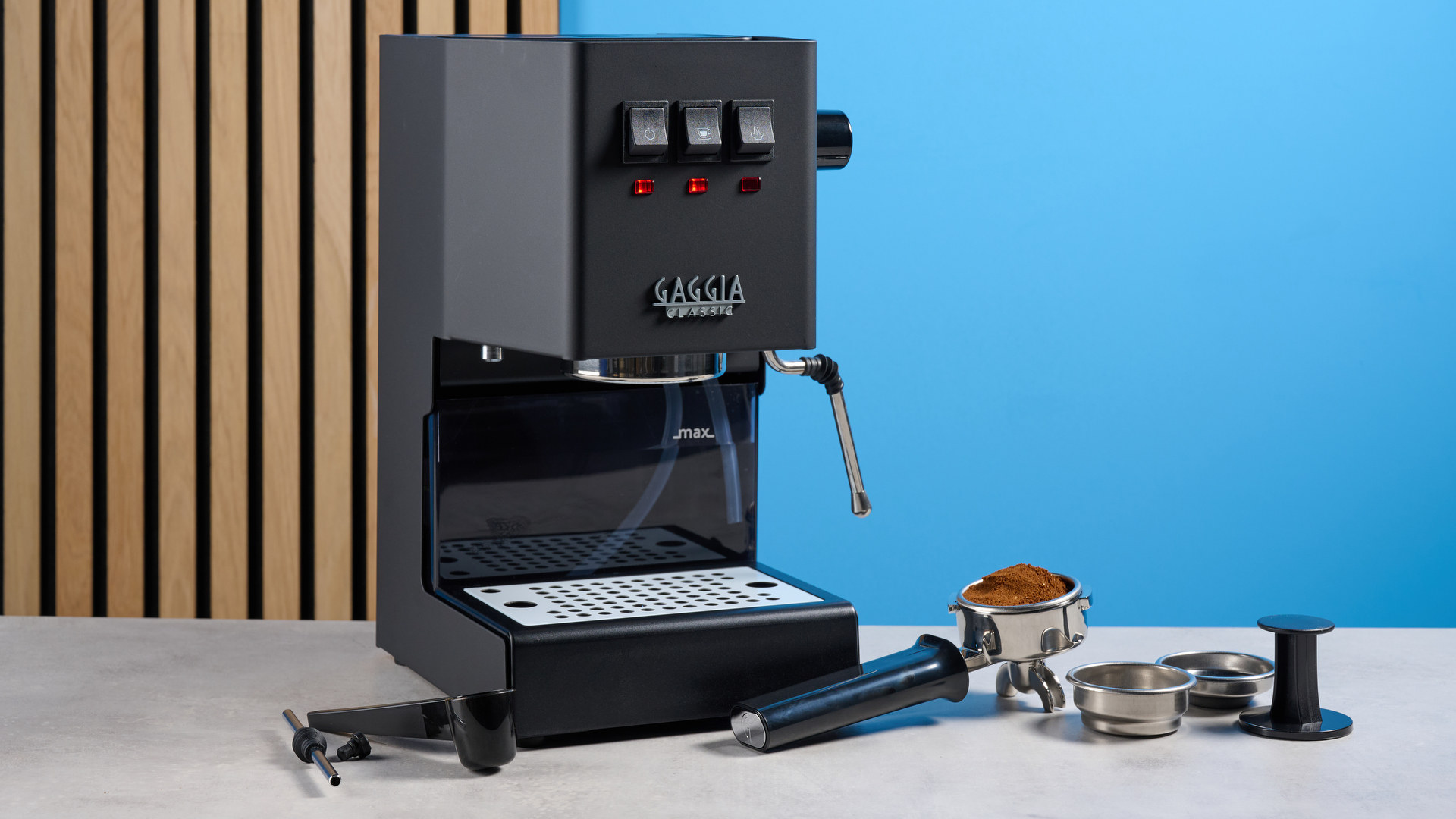 The Gaggia Classic E24 Evo Pro with its accessories against a blue background and on a stone surface