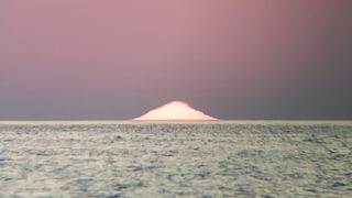 A mirage makes the sun look like a triangle as it sets beneath the horizon