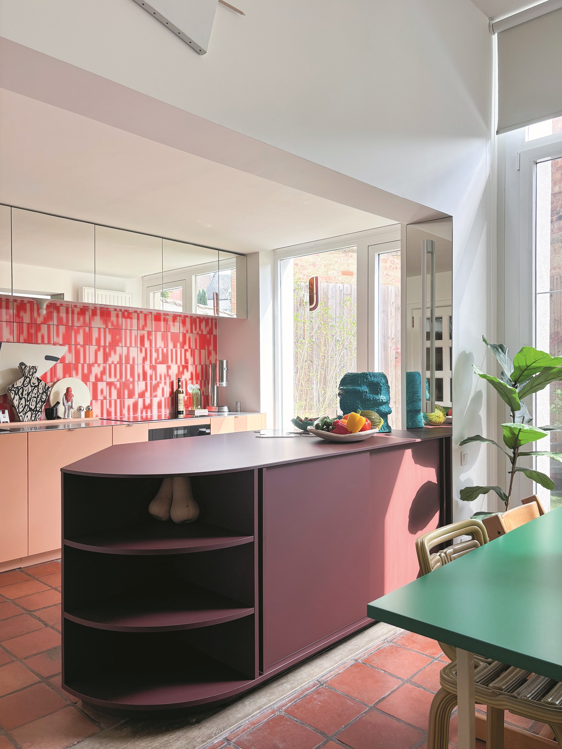 kitchen with terracotta floor tiles, red patterned backsplash, burgundy angular kitchen island, and mirrored cabinets