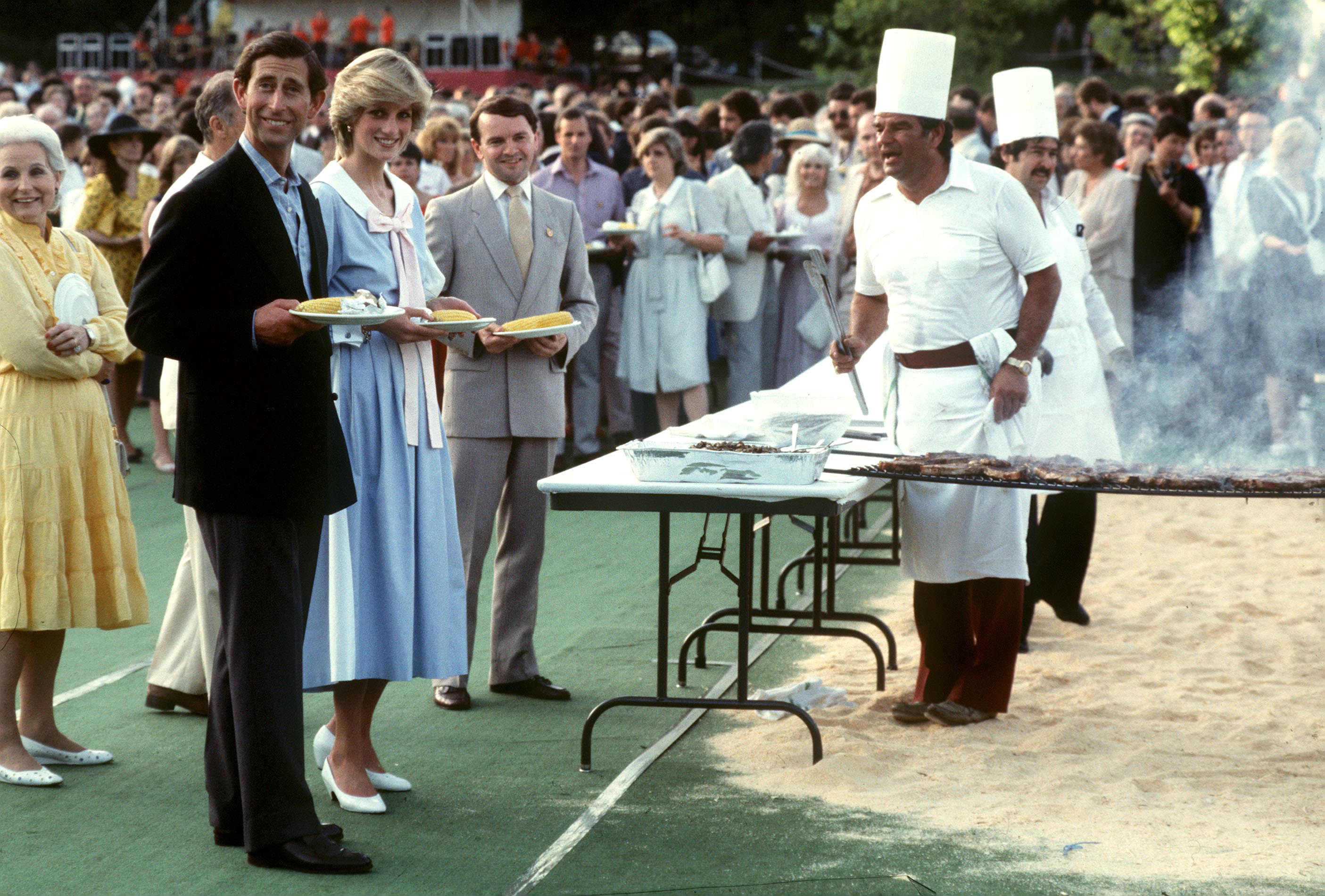 Prince Charles and Princess Diana holding plates of food at a BBQ