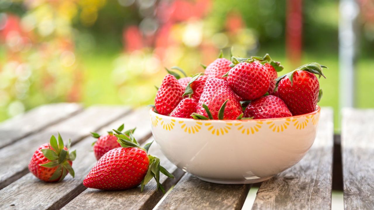 Red strawberries in a white bowl on a wooden table outside