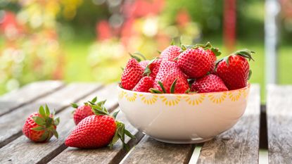 Red strawberries in a white bowl on a wooden table outside