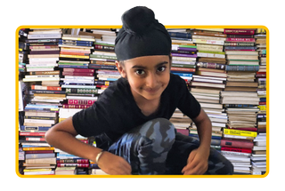 Image of a young boy, Anaik Sachdev, sitting in front of a pile of books