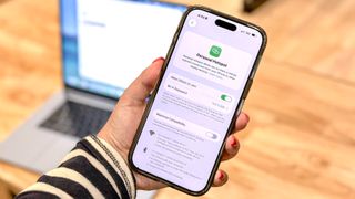 A person holding up an iPhone in front of a MacBook showing off iOS' Personal Hotspot feature