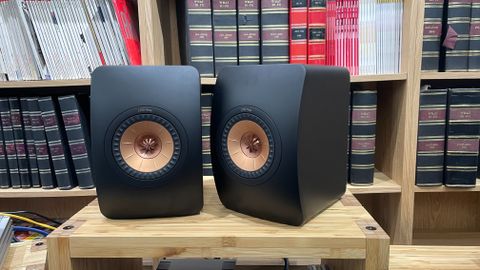 KEF LS50 Meta stereo speakers on wooden equipment rank with books in background
