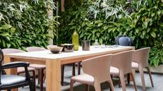 outdoor timber dining table with timber chairs and black carver chairs, plants all over the walls, and bowls and wine bottle on table