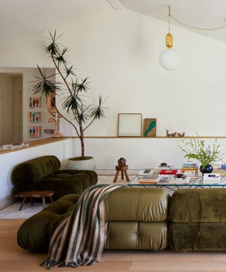 neutral space with a large green leather sectional couch, artwork and plants