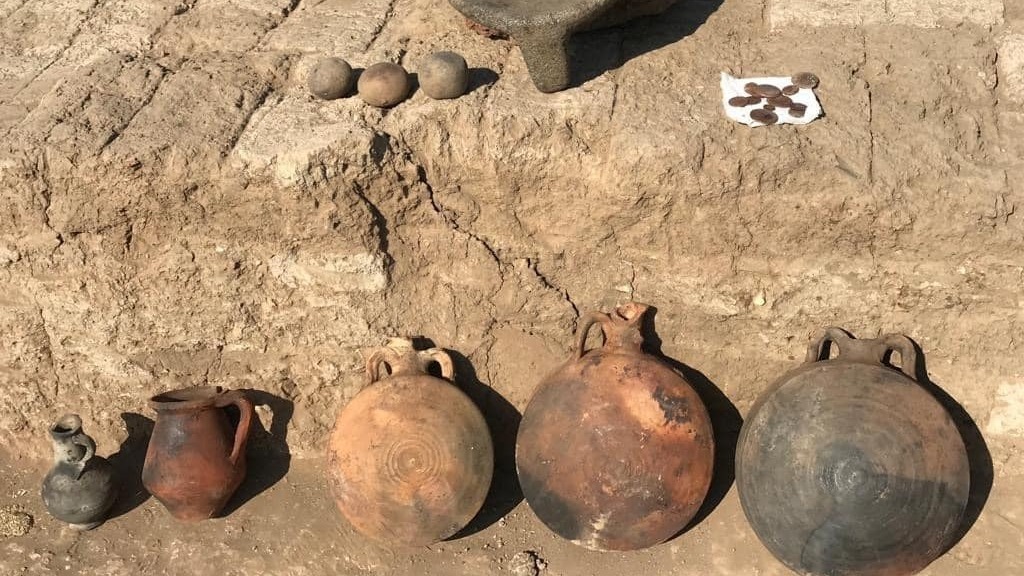 A photo showing ceramic vessels, coins and ball-like grinding artifacts that were found at the site.