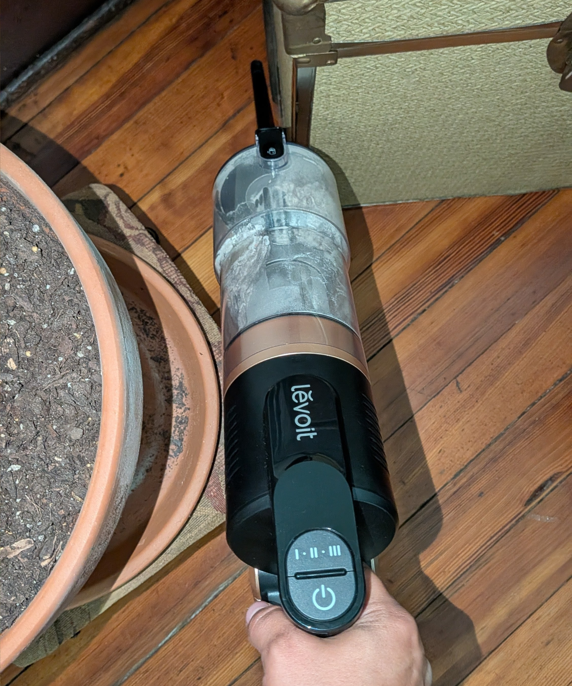 Using the Levoit VortexIQ Pro as a handheld vacuum cleaner with the 2-in-1 crevice tool to clean in a tight space between a potted plant and a box.