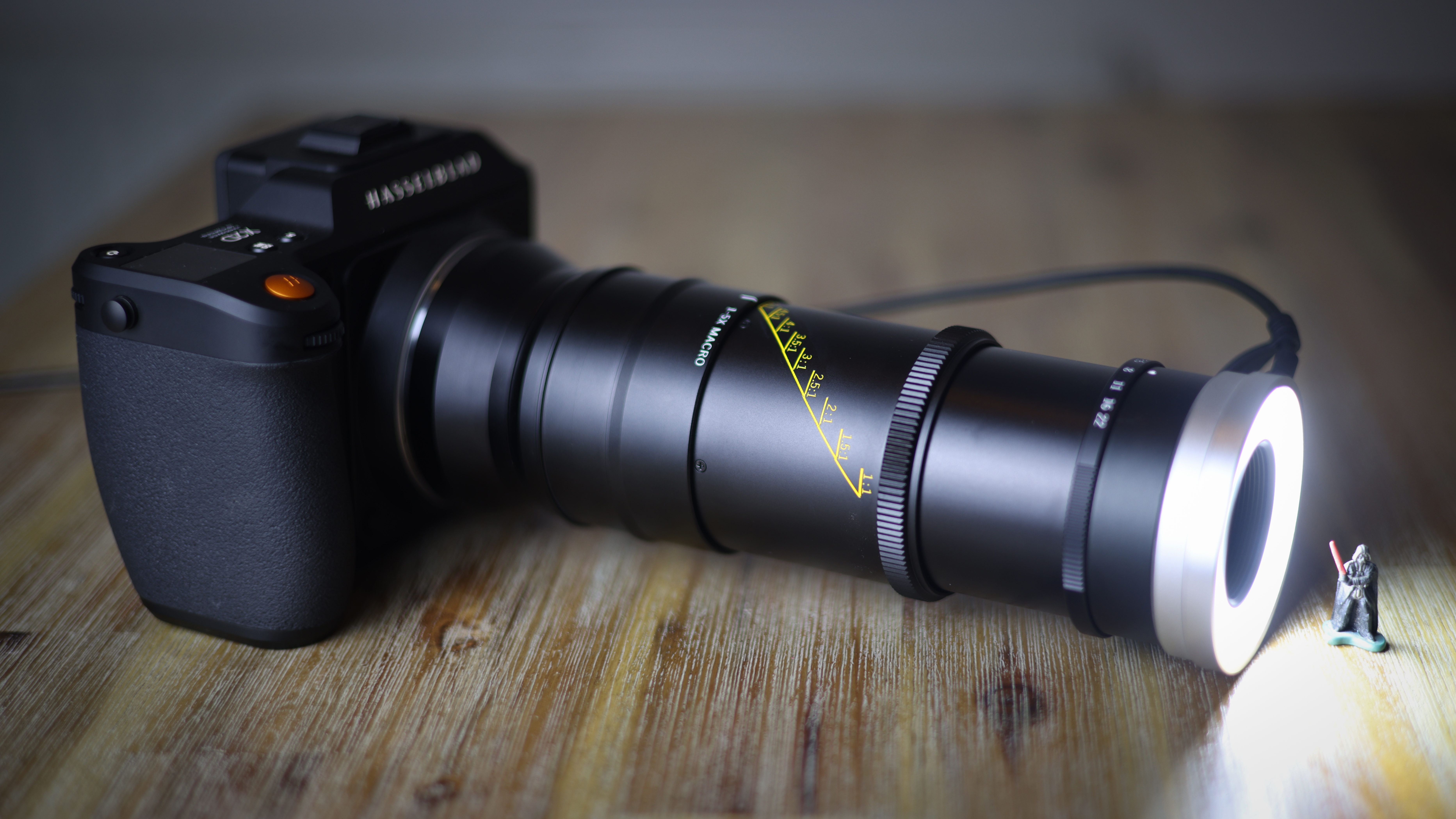 Mitakon 55mm f/2.8 1-5x Macro on a wooden surface, with the lighting attachment