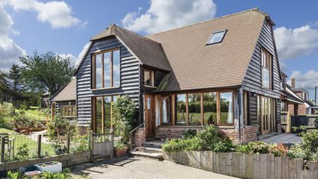 Timber cladding and render weatherboard on a large barn-style home with a green garden to the left and patio to the right