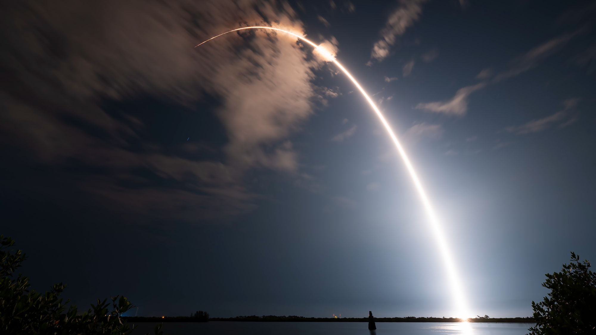 Un lancement de fusée coupe un arc orange dans le ciel nocturne sombre sur cette image à exposition longue.