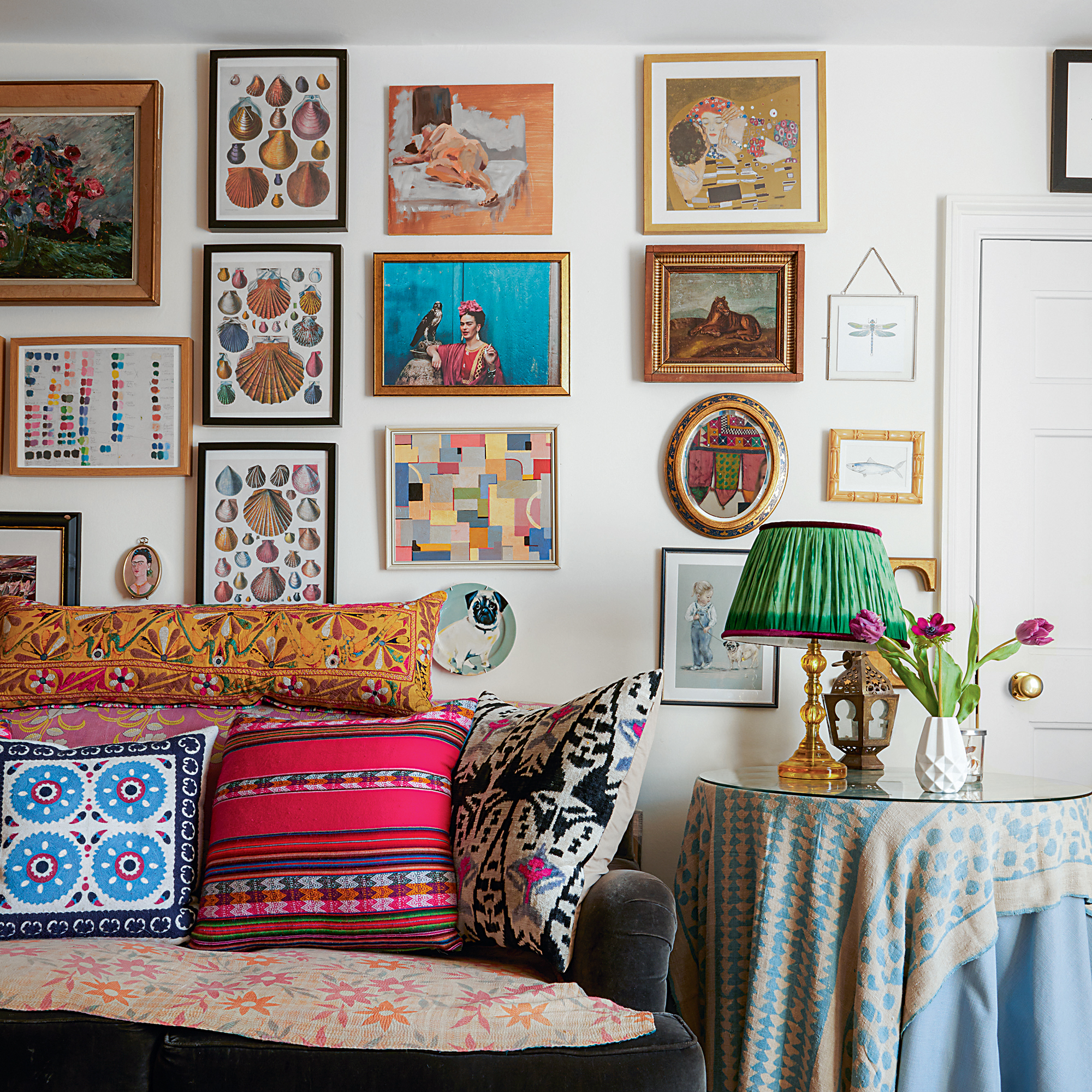 Gallery wall of mixed artwork behind a sofa covered in eclectic scatter cushions