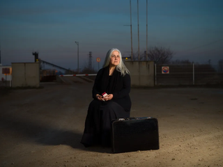 A displaced woman sitting on a suitcase with all her worldly possessions, about to light up a cigarette