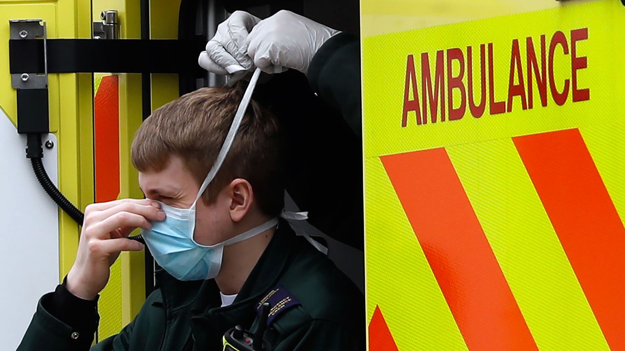 A paramedic gets help fitting a face mask during the coronavirus pandemic