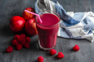 Apple, berries and mint smoothie in a glass with a pink straw and berries and an apple scattered around the glass