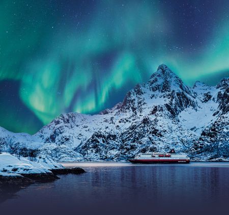 cruise ship next to snowy mountain underneath the northern lights