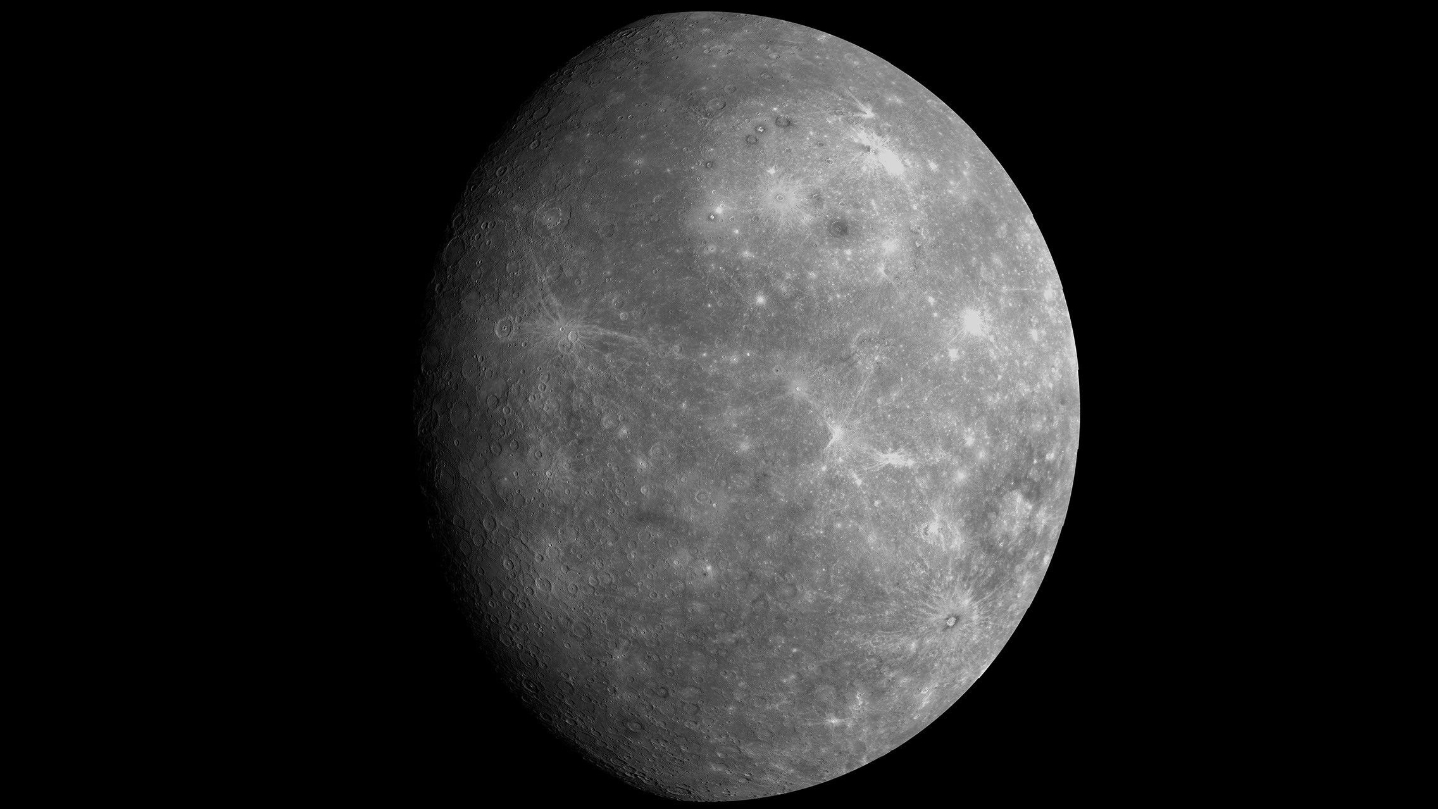 A picture of a grey, rocky, cratered planet against a black background. The left extreme of the world is bathed in shadow and white spots are visible on the surface where bright material has been thrown out by recent asteroid impacts.
