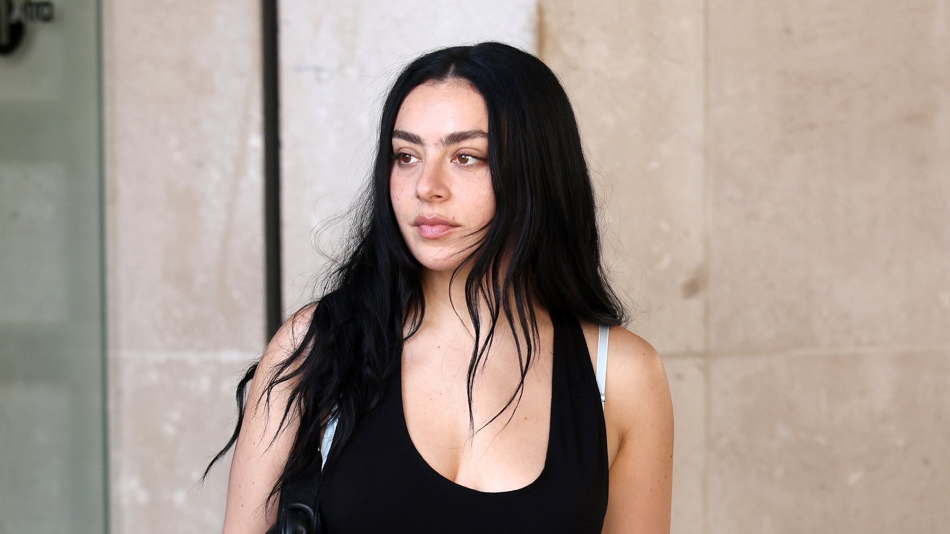 Charli XCX wears a black mini dress with pointed-toe pink crocodile pumps and has long black hair