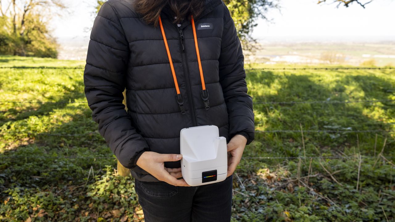 A female photographer holds the Polaroid Flip instant camera in a sunny field