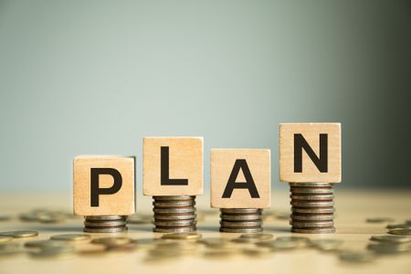 Wooden Block Letters Spelling PLAN Placed on Stacked Coins