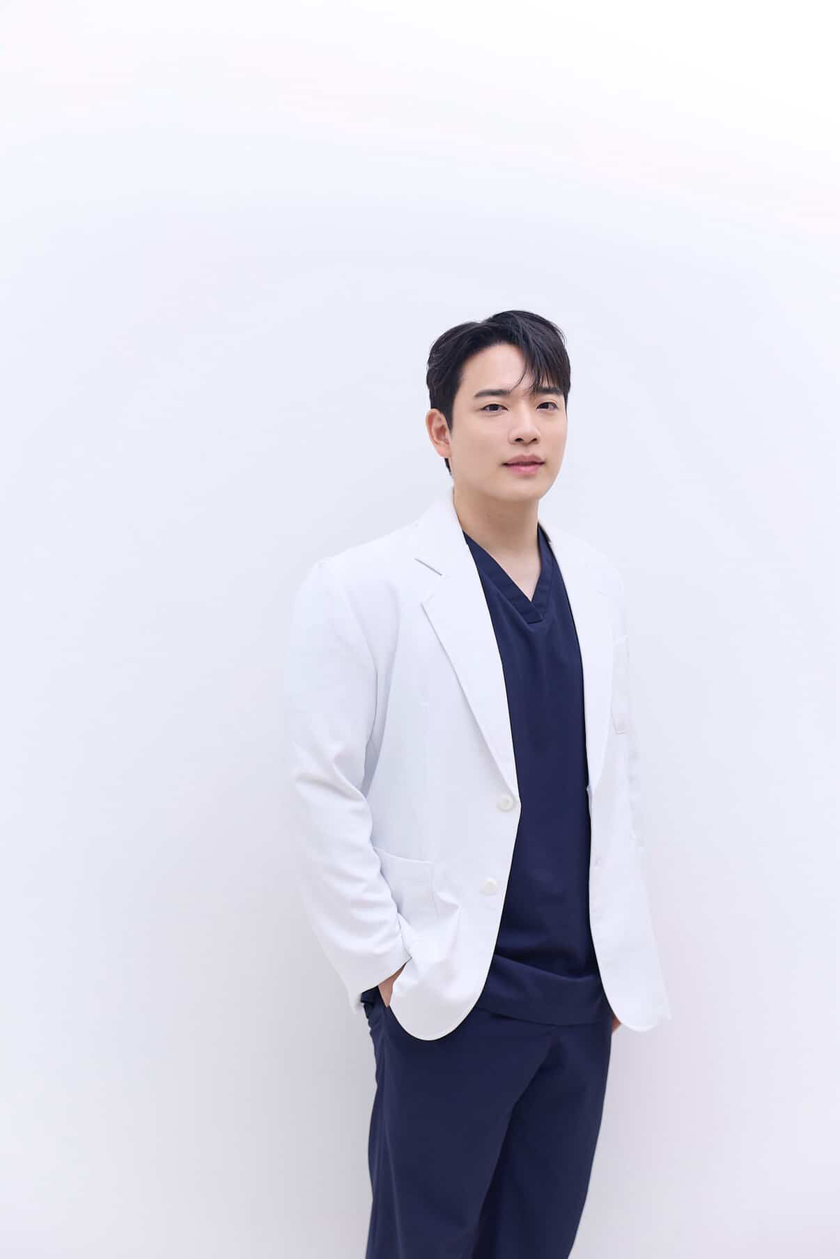 a young korean man in blue scrubs and a white lab coat